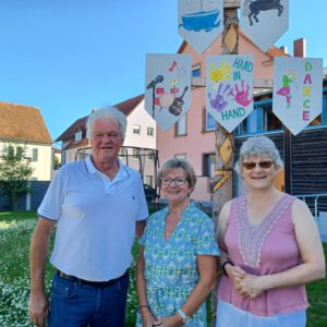 Ein Ehepaar und eine Frau im Garten vor dem Maibaum.