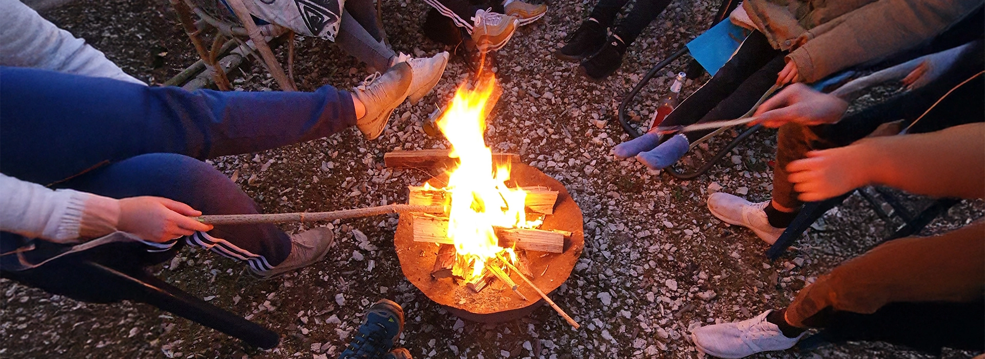 Kinder sitzen und halten Stöcke um ein Lagerfeuer.