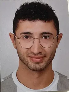 Ein Portrait von einem jungen Mann mit Brille. Er lächelt.