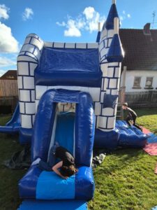 Eine blaue Hüpfburg in einem Garten, auf der Kinder rumtollen.