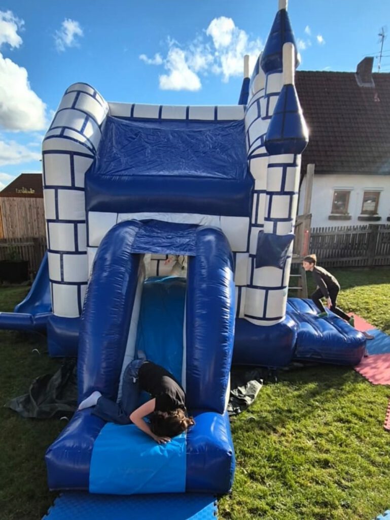 Eine blaue Hüpfburg in einem Garten, auf der Kinder rumtollen.