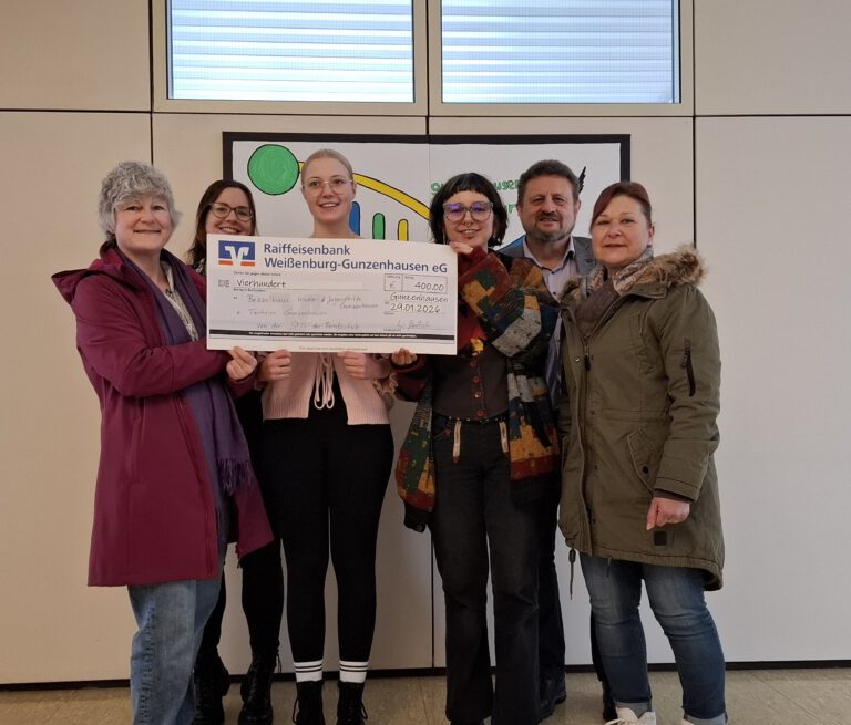 Sechst Personen stehen in einem Gang mit einem Scheck vor sich zu einer Spende