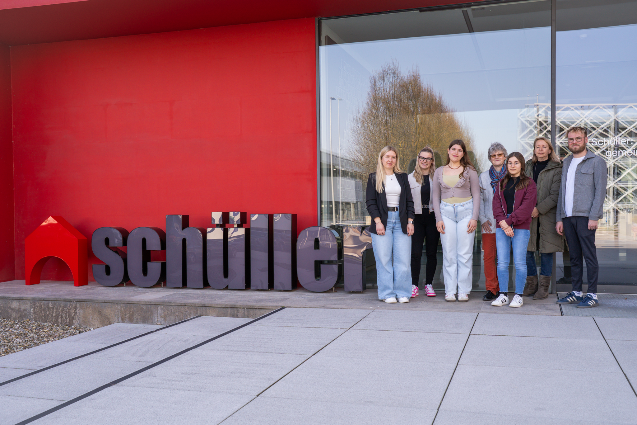 Sieben Personen stehen draußen vor dem "Schüller" Logo.
