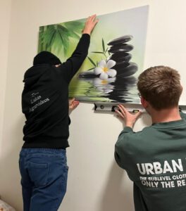 Zwei junge Männer hängen mit Hilfe einer Wasserwaage ein Bild auf.