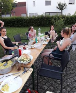 Mehrere junge Frauen sitzen im Garten und essen Gegrilltes.